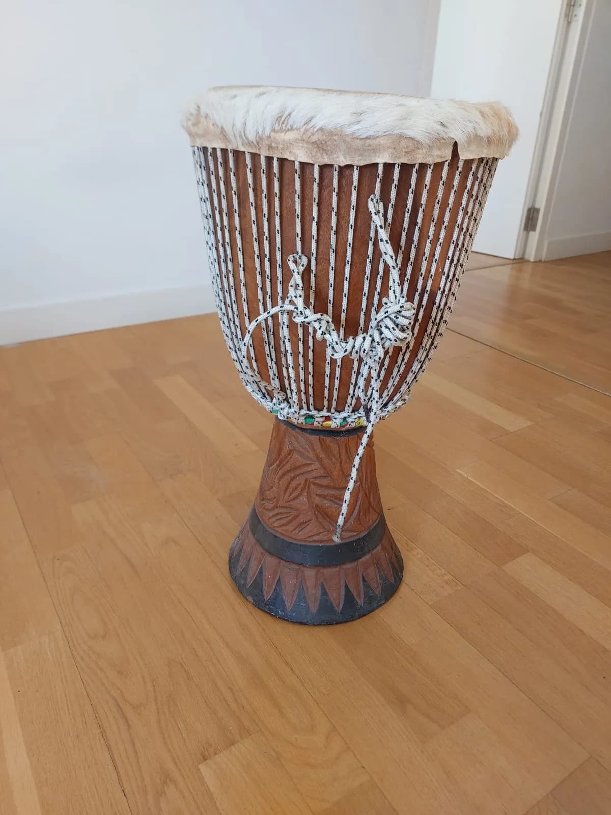 Djembe de segunda mano de madera clara con parche de piel blanca, cuerdas y base tallada.